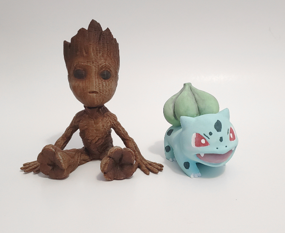 Two 3D printed figures, on left is baby groot painted in oil paints and on right a pokemon named bulbasaur that is painted in acrylic paints. 